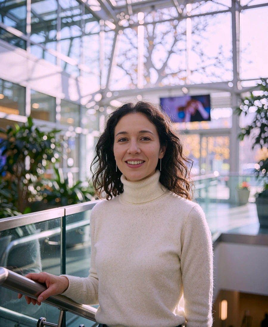 Woman standing inside a bright glass atrium office building in Seattle with steel framing and greenery blurred behind her
