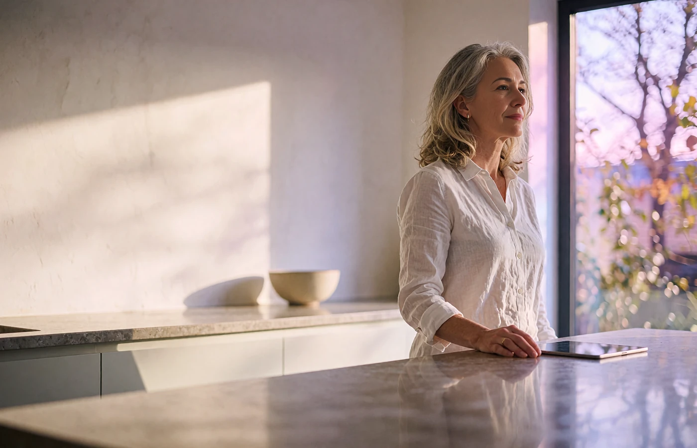 Elegant woman standing at a bright kitchen island, pausing beside a tablet after reviewing her monthly allowance budget