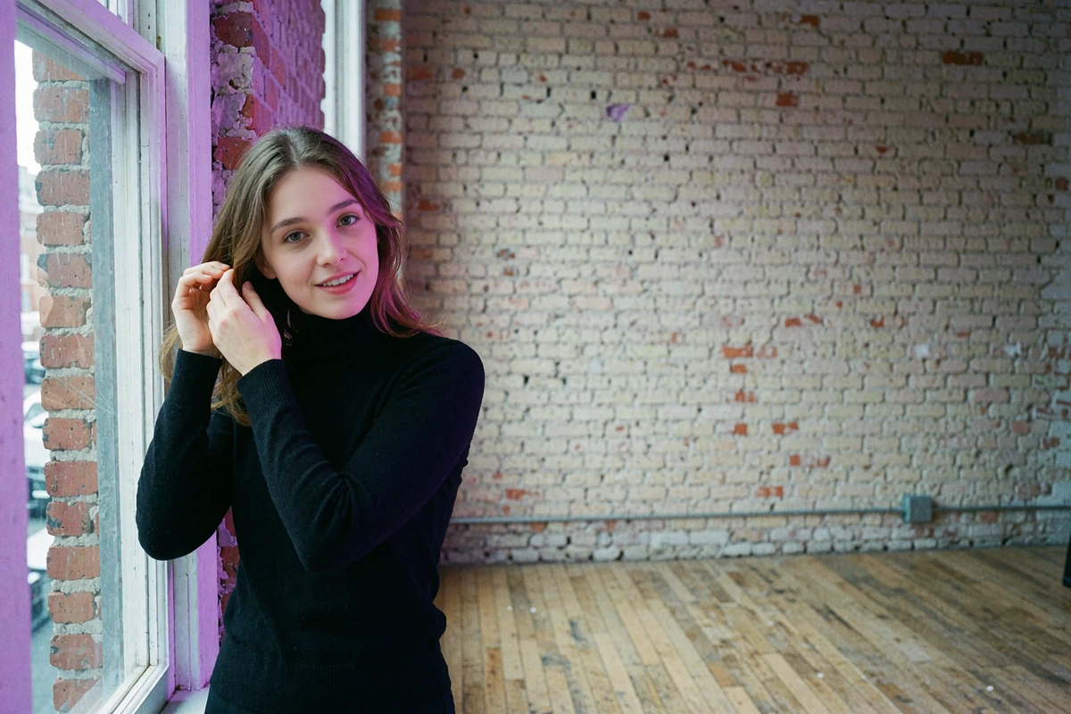 Young woman in a black turtleneck beside a tall studio window in a converted Boston brick loft